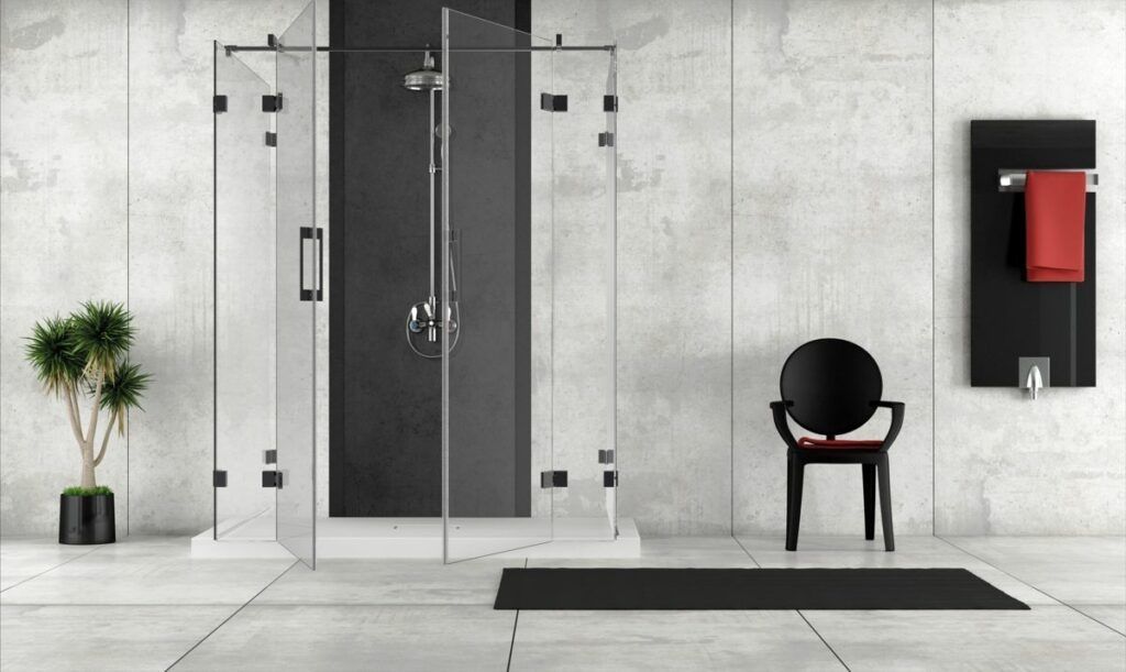 Modernes Badezimmer mit Glasdusche, schwarzem Stuhl, Handtuchhalter und Topfpflanze vor einer grauen Betonwand.