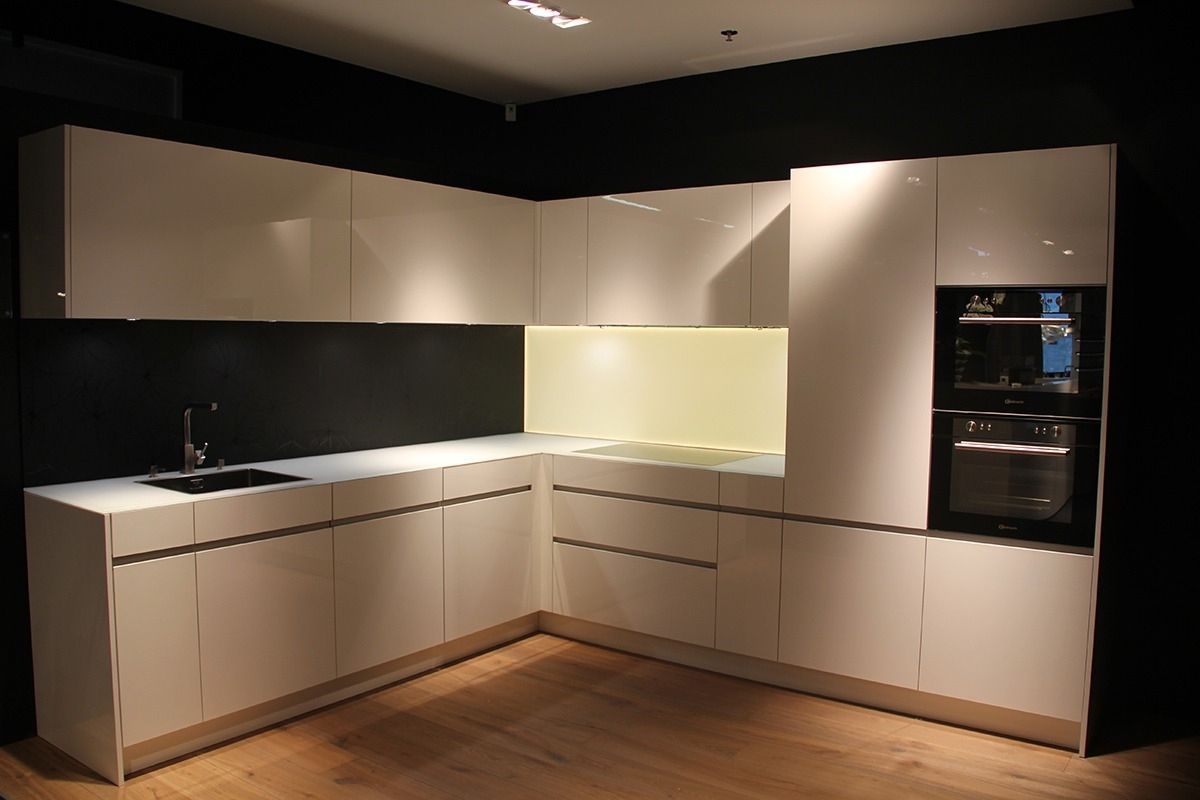 Moderne weisse Küche mit Hochglanzschränken, Einbaubackofen und schwarzen Arbeitsplatten vor dunklen Wänden.