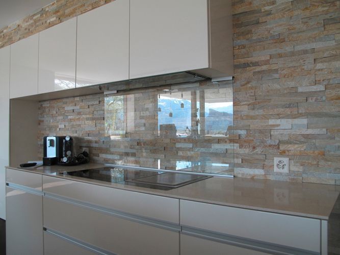 Moderne Küche mit hellen Schränken, Steinrückwand und Kochfeld.