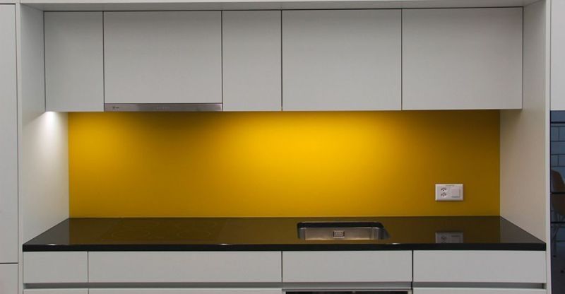 Gelber Fliesenspiegel in einer Küche mit weißen Ober- und Unterschränken und schwarzer Arbeitsplatte.