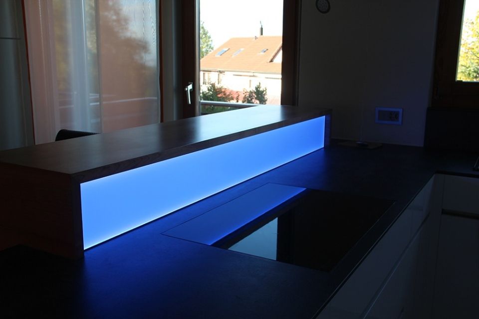 Küchenarbeitsplatte mit eingebautem, blau beleuchtetem Bedienfeld und integriertem Kochfeld. Fenster im Hintergrund.