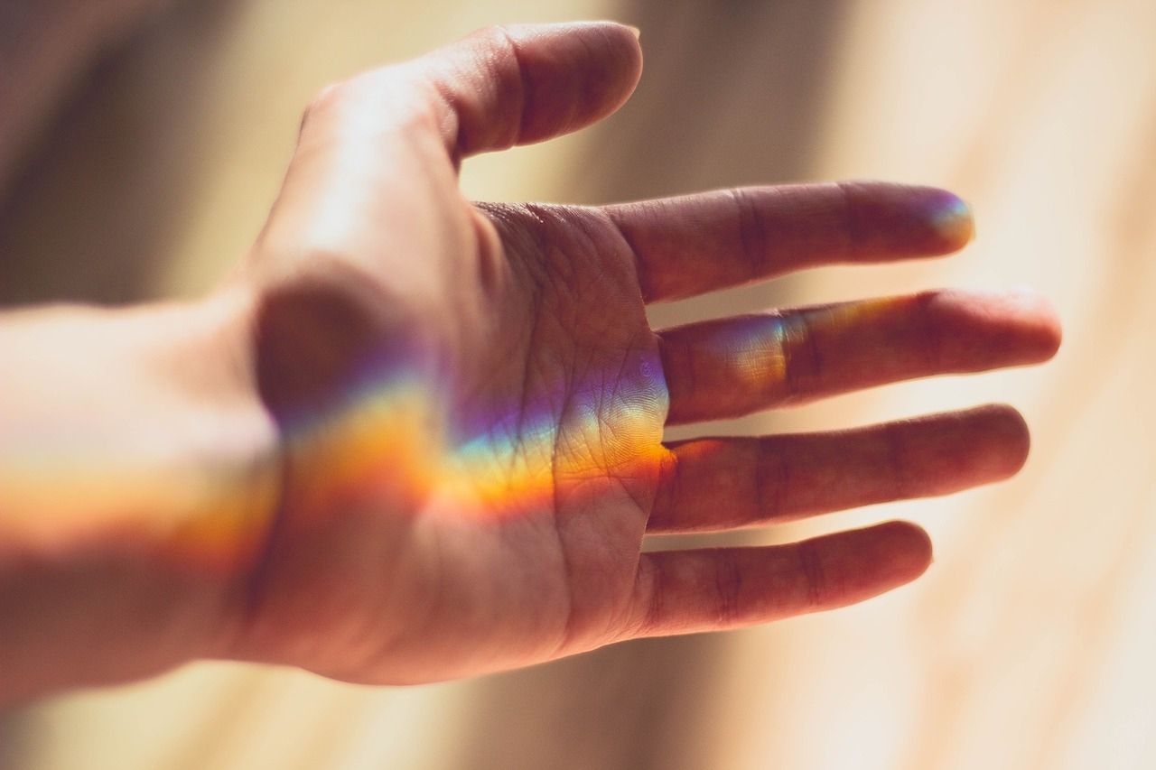 Eine Hand fängt ein Regenbogenlicht ein, Farben fallen über Handfläche und Finger, warme Atmosphäre.