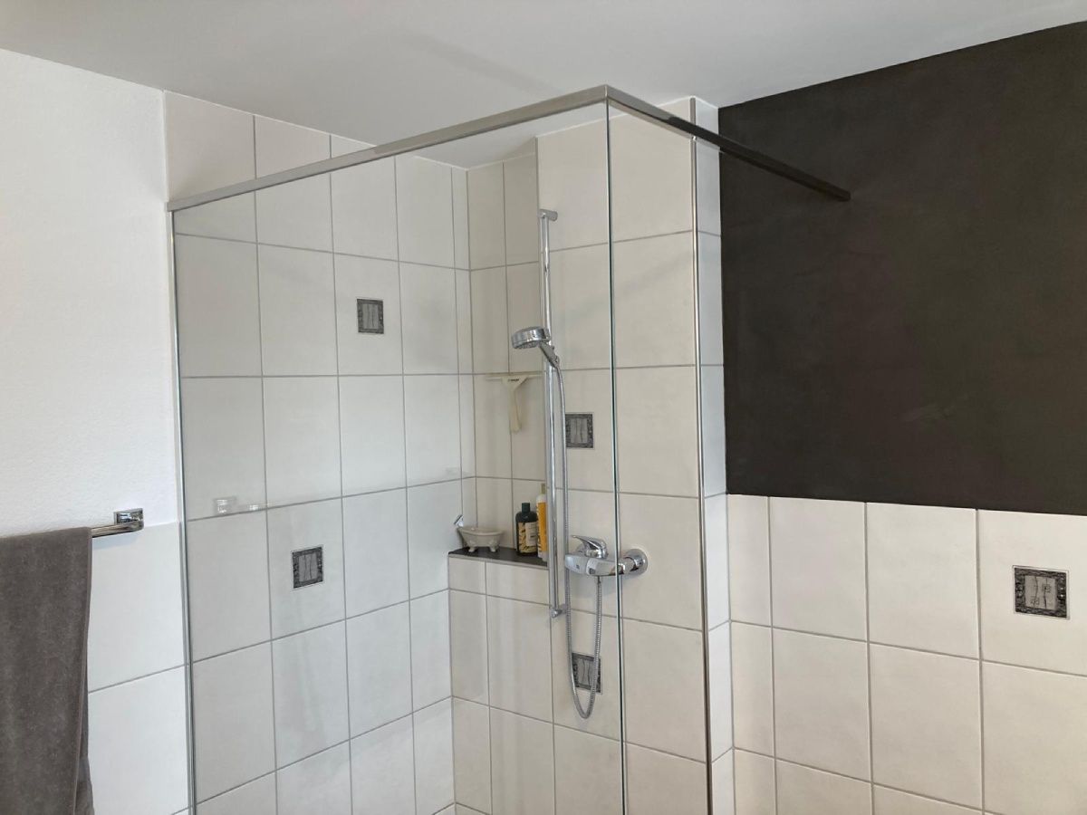 Duschkabine mit weiß gefliesten Wänden, Glastür und Chromarmaturen.