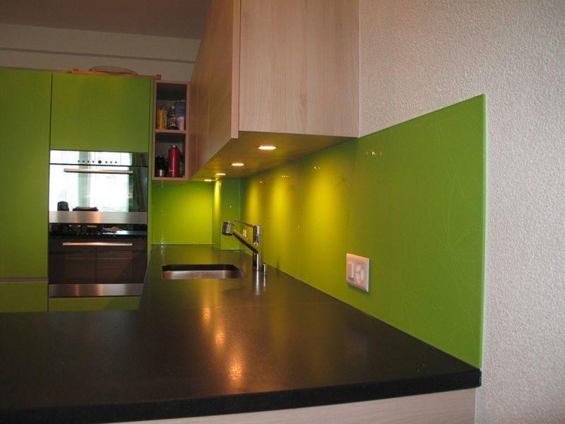 Moderne Küche mit limettengrünem Fliesenspiegel, dunkler Arbeitsplatte, silberner Armatur und integrierter Beleuchtung.