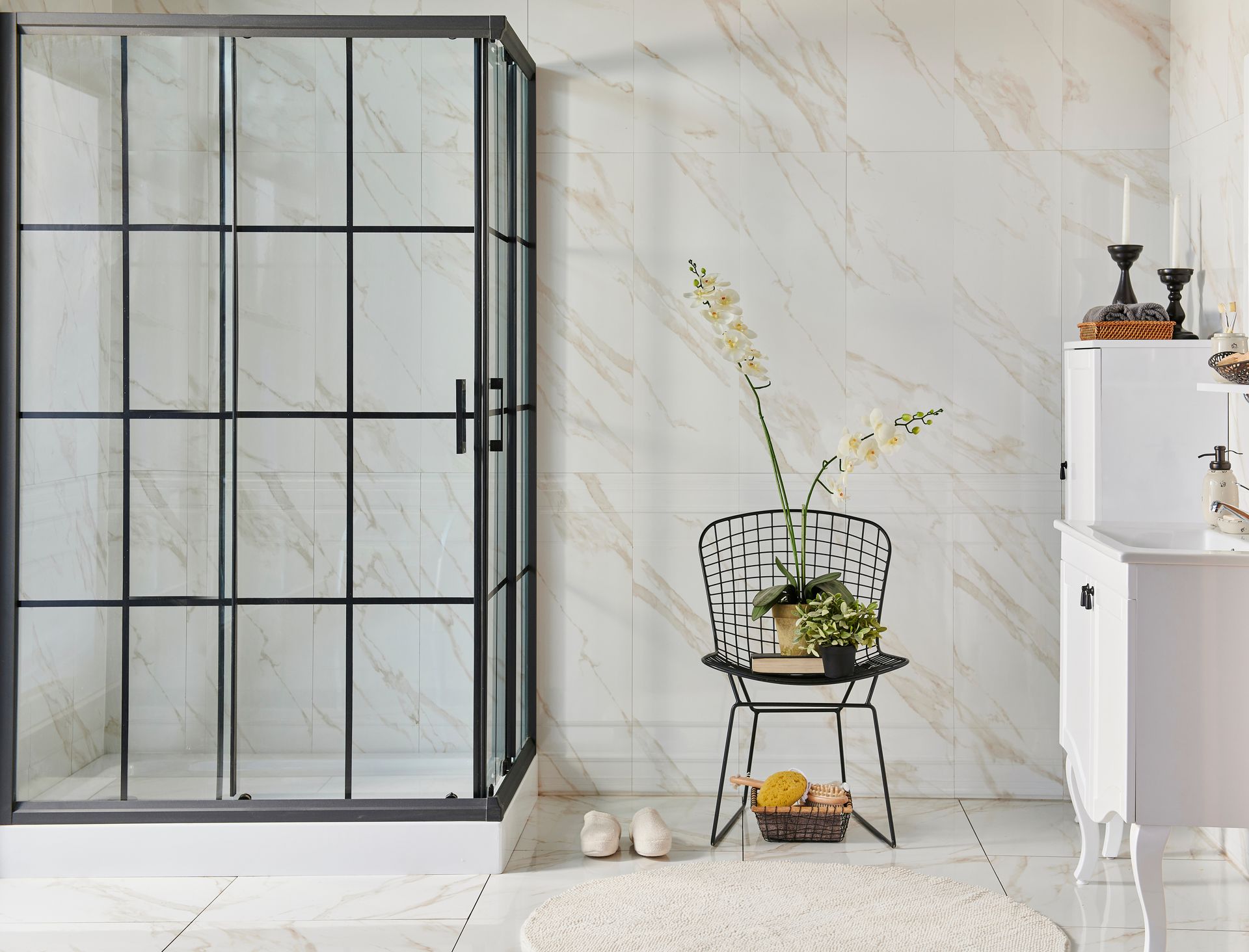 Eine Duschkabine mit schwarzem Rahmen und marmorähnlichen Fliesen in einem Badezimmer. Daneben steht ein Stuhl mit Pflanzen.