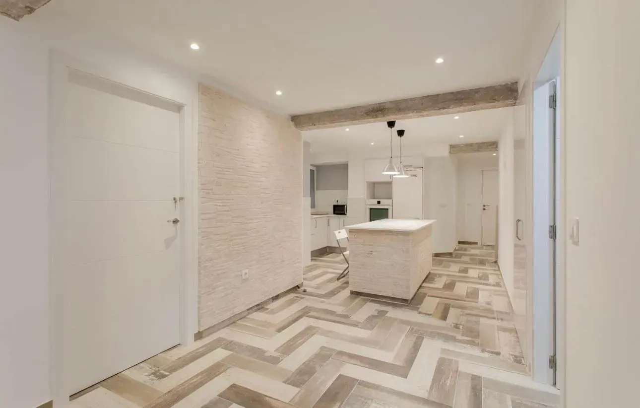 Vista interior de una cocina moderna con paredes blancas, isla y pisos de madera.