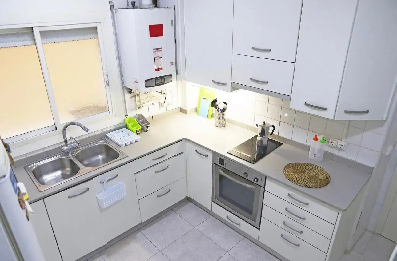 Cocina blanca con gabinetes, horno y fregadero. Incluye ventana y calentador de agua.