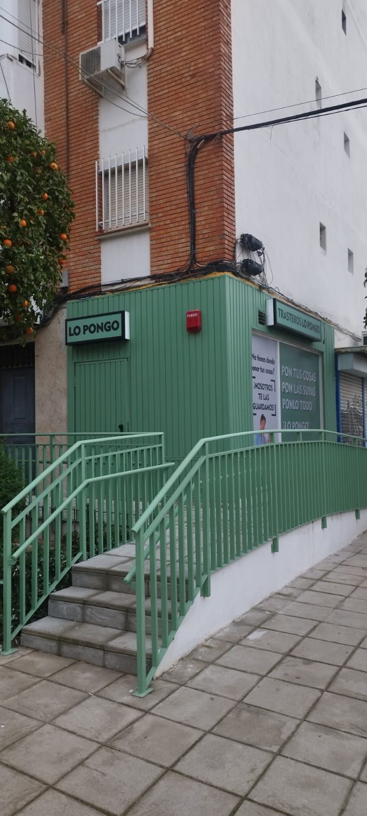 Edificio verde con escaleras y rampa, al lado de un edificio de ladrillo.