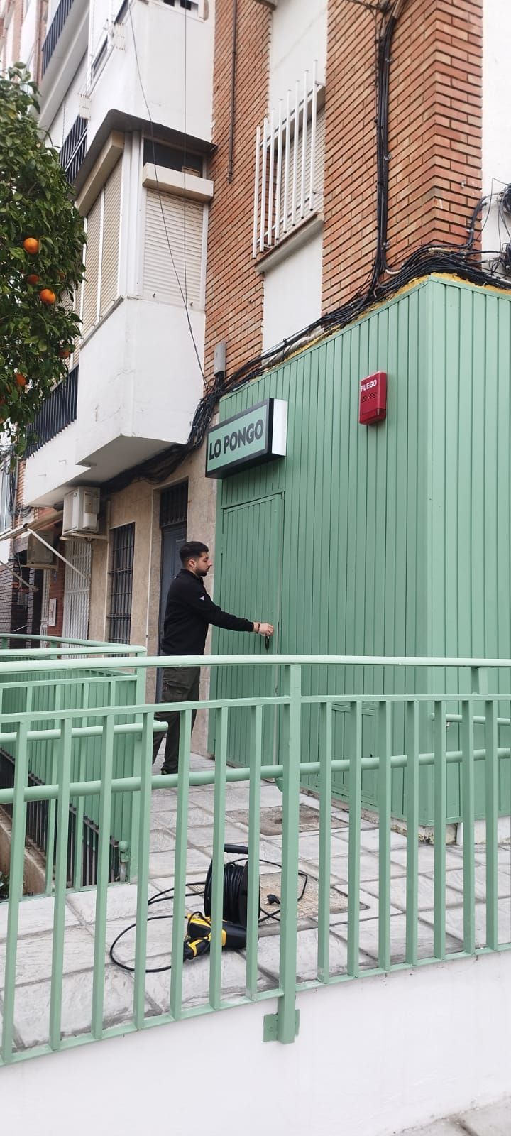 Un hombre toca un muro verde, frente a una valla verde. Un cartel sobre el muro dice