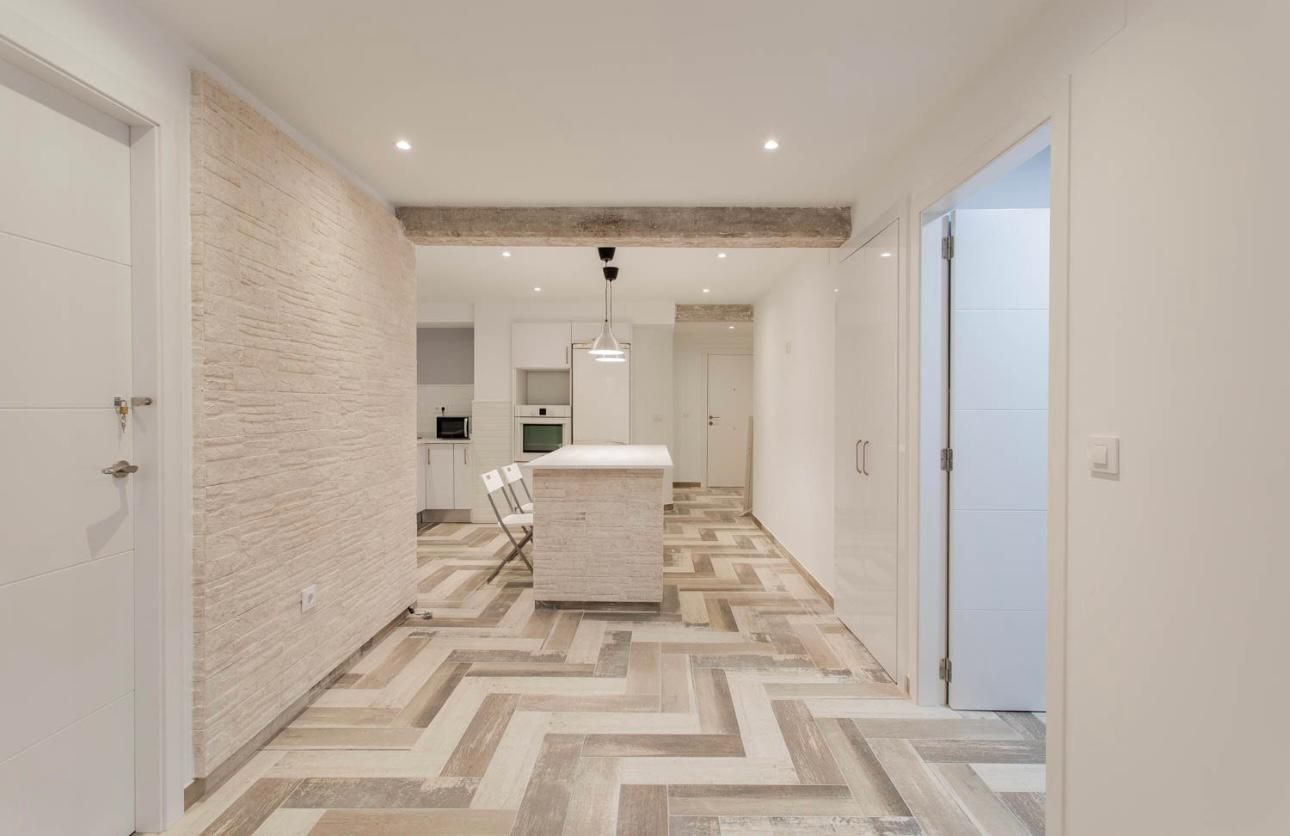 Un pasillo con suelo de espiga da acceso a una cocina blanca. Hay una pared de ladrillo a la izquierda.