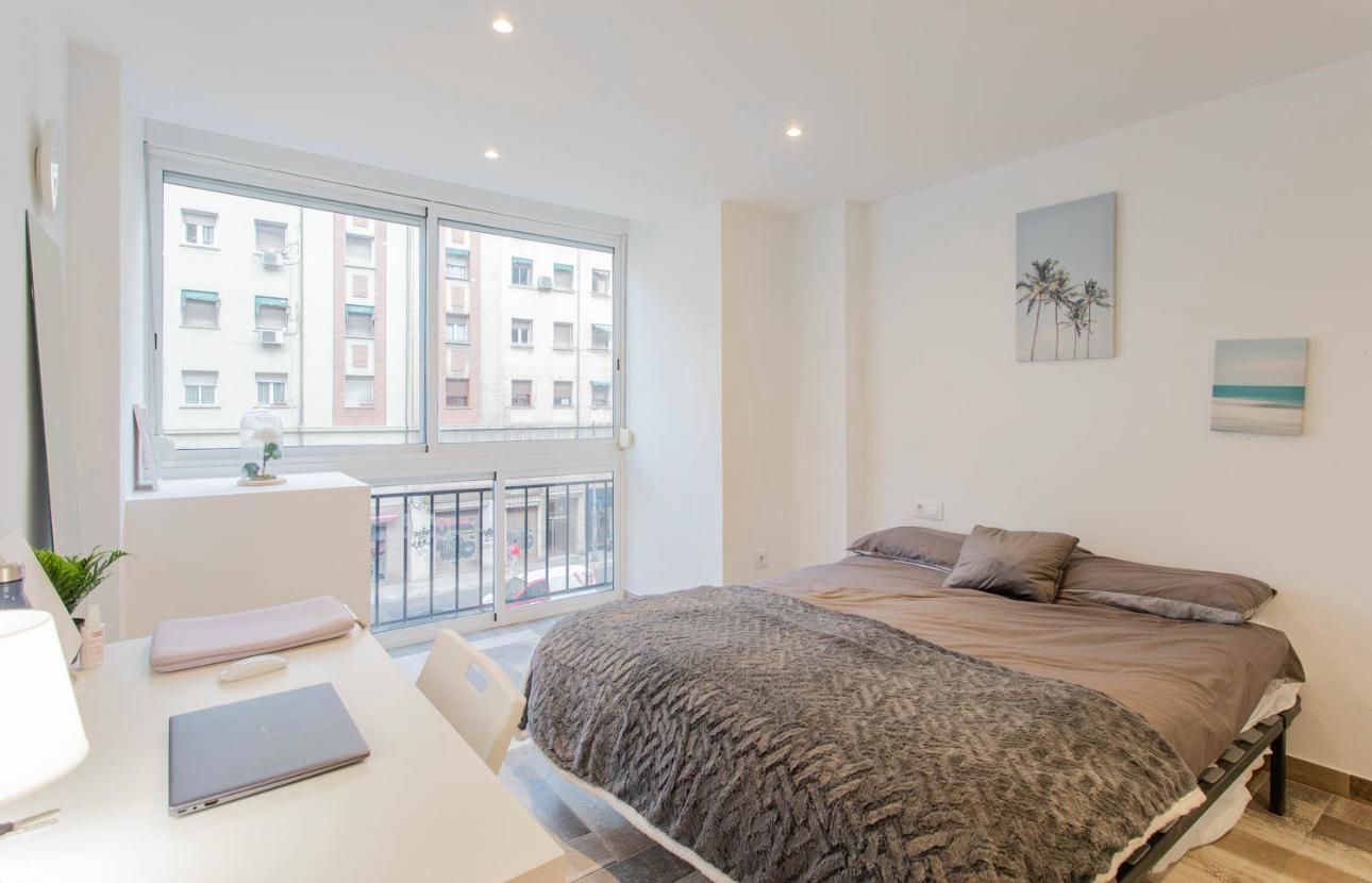 Dormitorio con cama, escritorio, ventana con vistas a los edificios de la ciudad y obras de arte decorativas.