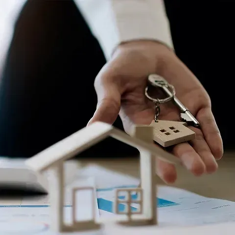 Una persona sostiene una maqueta de casa y llaves en su mano.