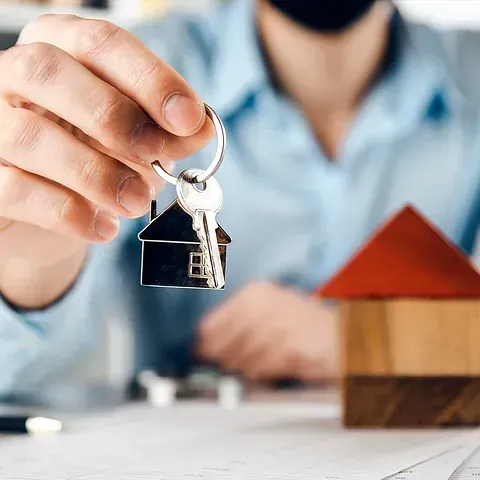 Un hombre sostiene una llave con una casa delante de una casa modelo.