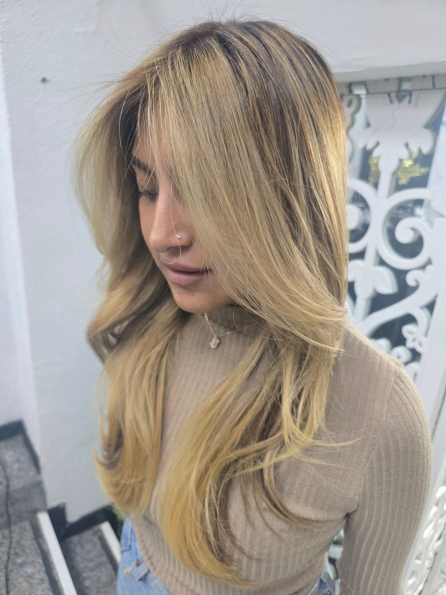 Una mujer con cabello largo y rubio y un anillo en la nariz está parada frente a una pared blanca.