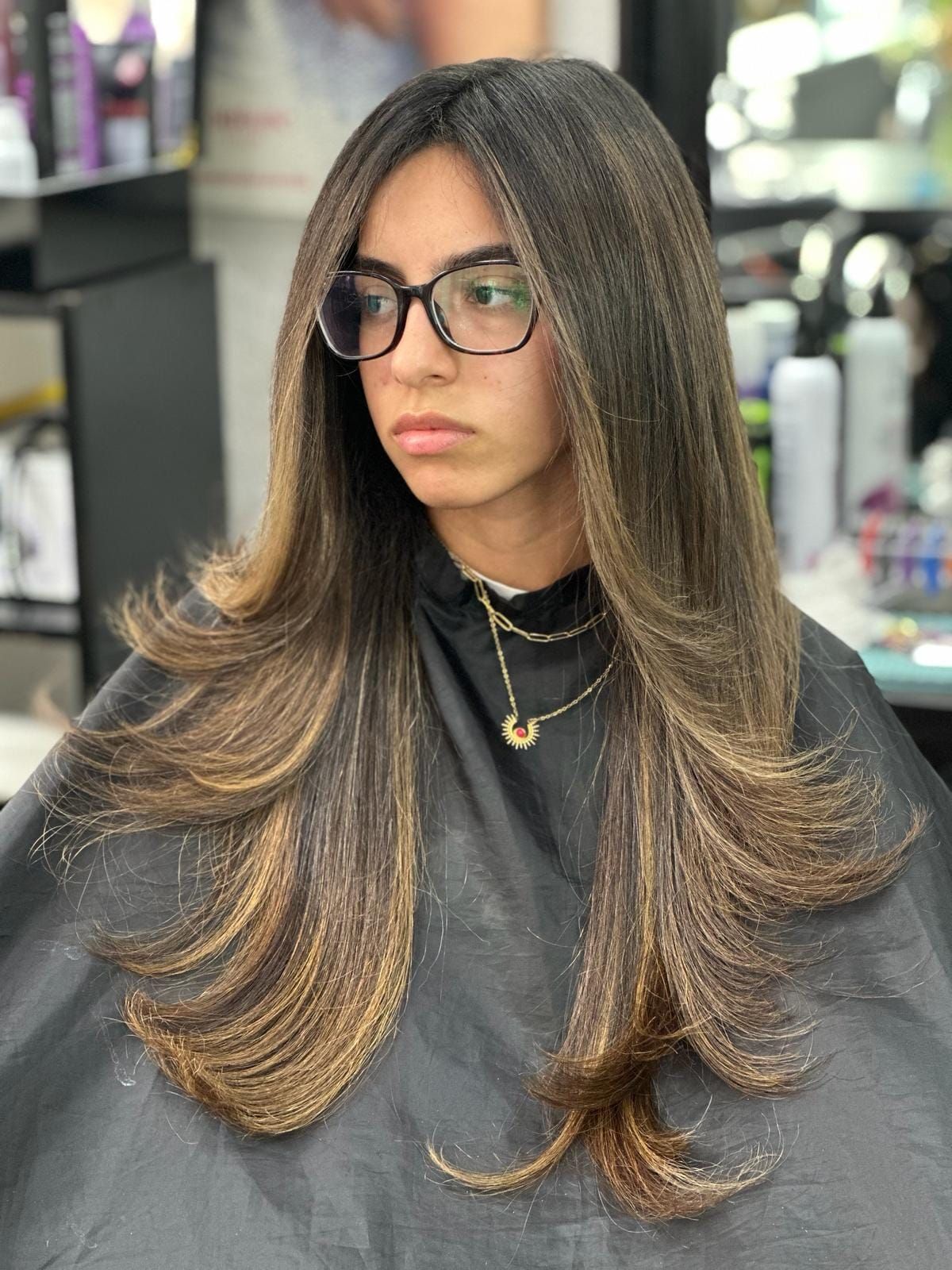 Una mujer con cabello largo y gafas se está cortando el pelo en una peluquería.