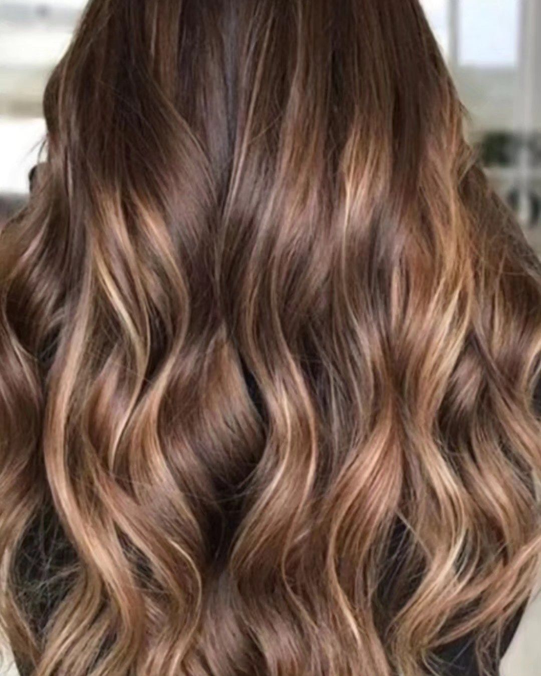 Una mujer con cabello castaño largo y ondulado lleva una camisa negra.