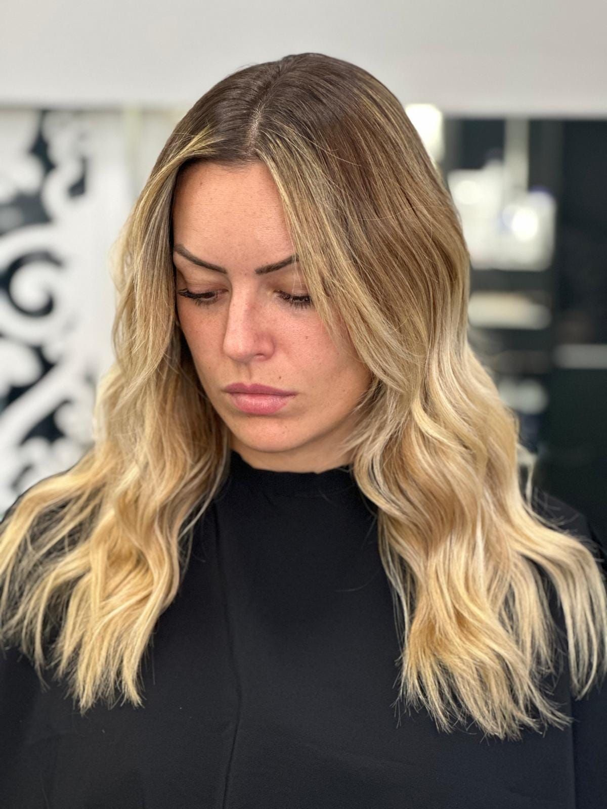 Una mujer con cabello rubio y una camisa negra mira hacia abajo.