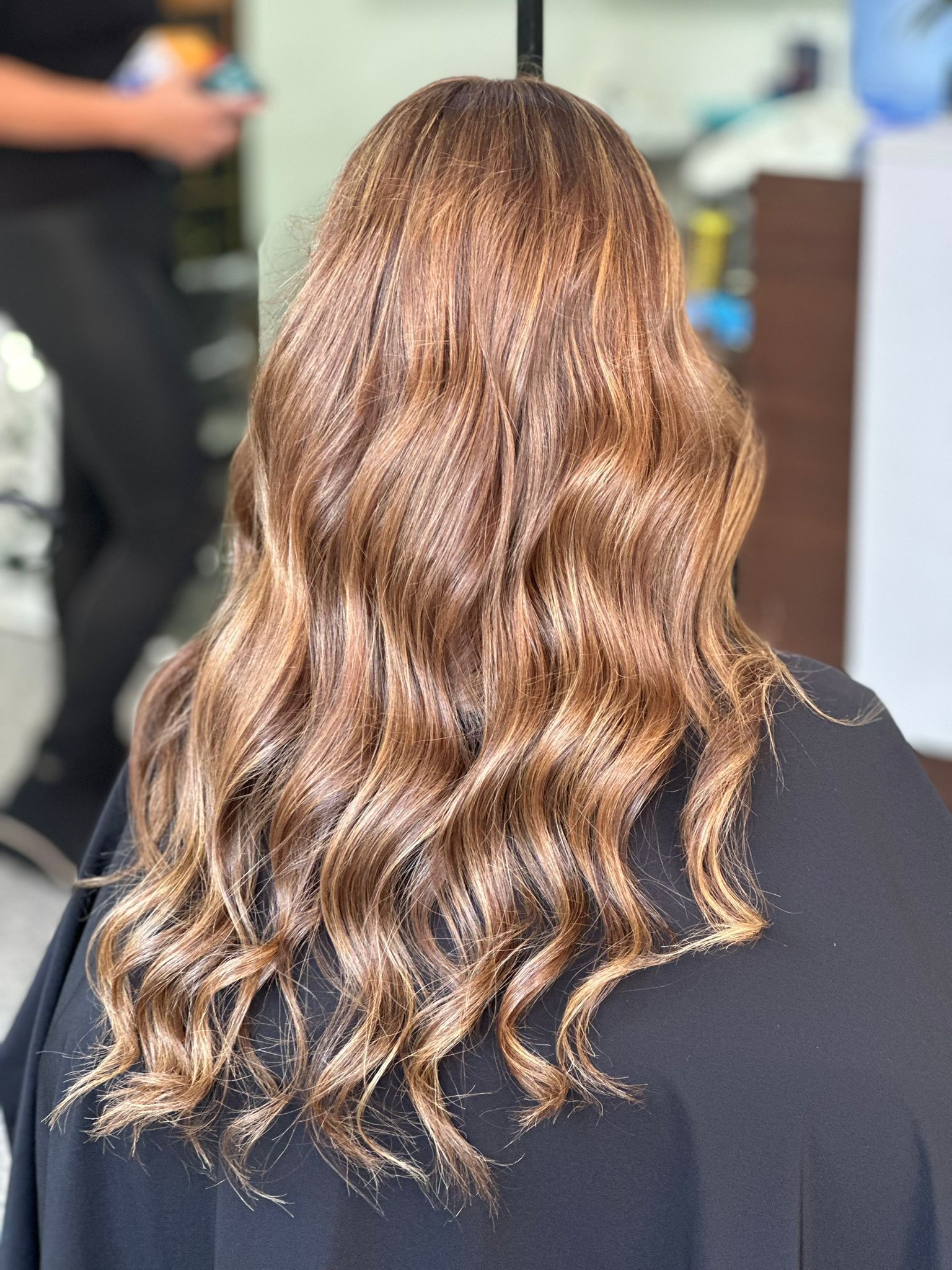 Una mujer con cabello largo y castaño está sentada en una silla en una peluquería.