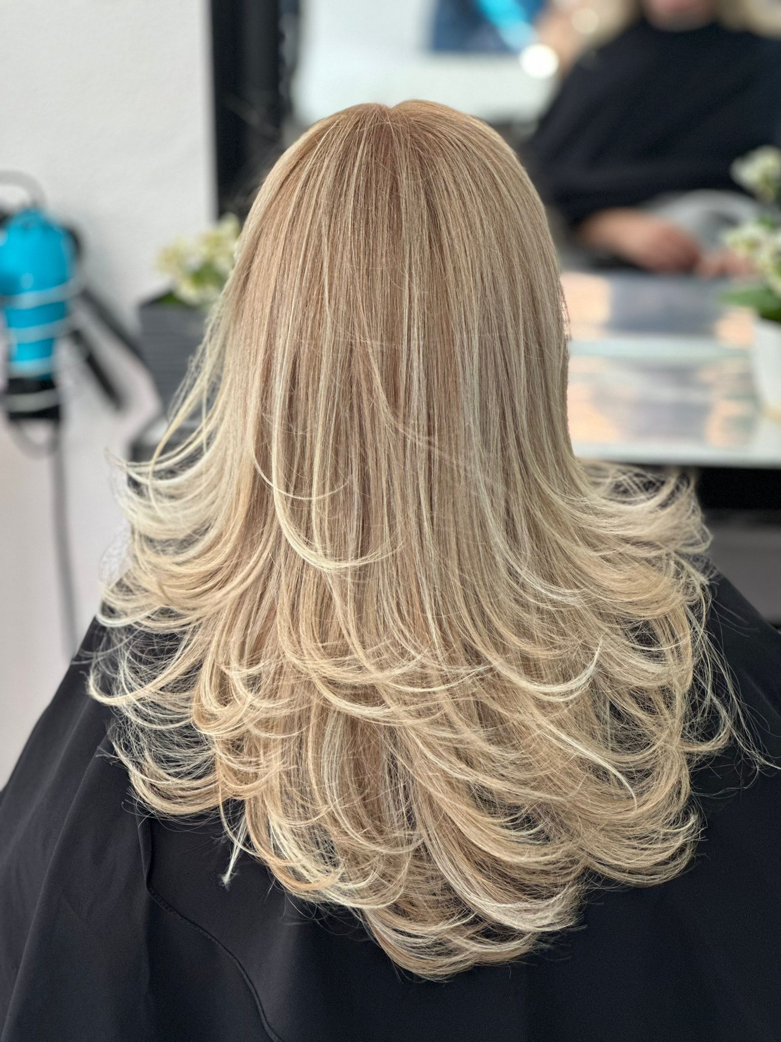 Una mujer con cabello largo y rubio está sentada en una silla en una peluquería.