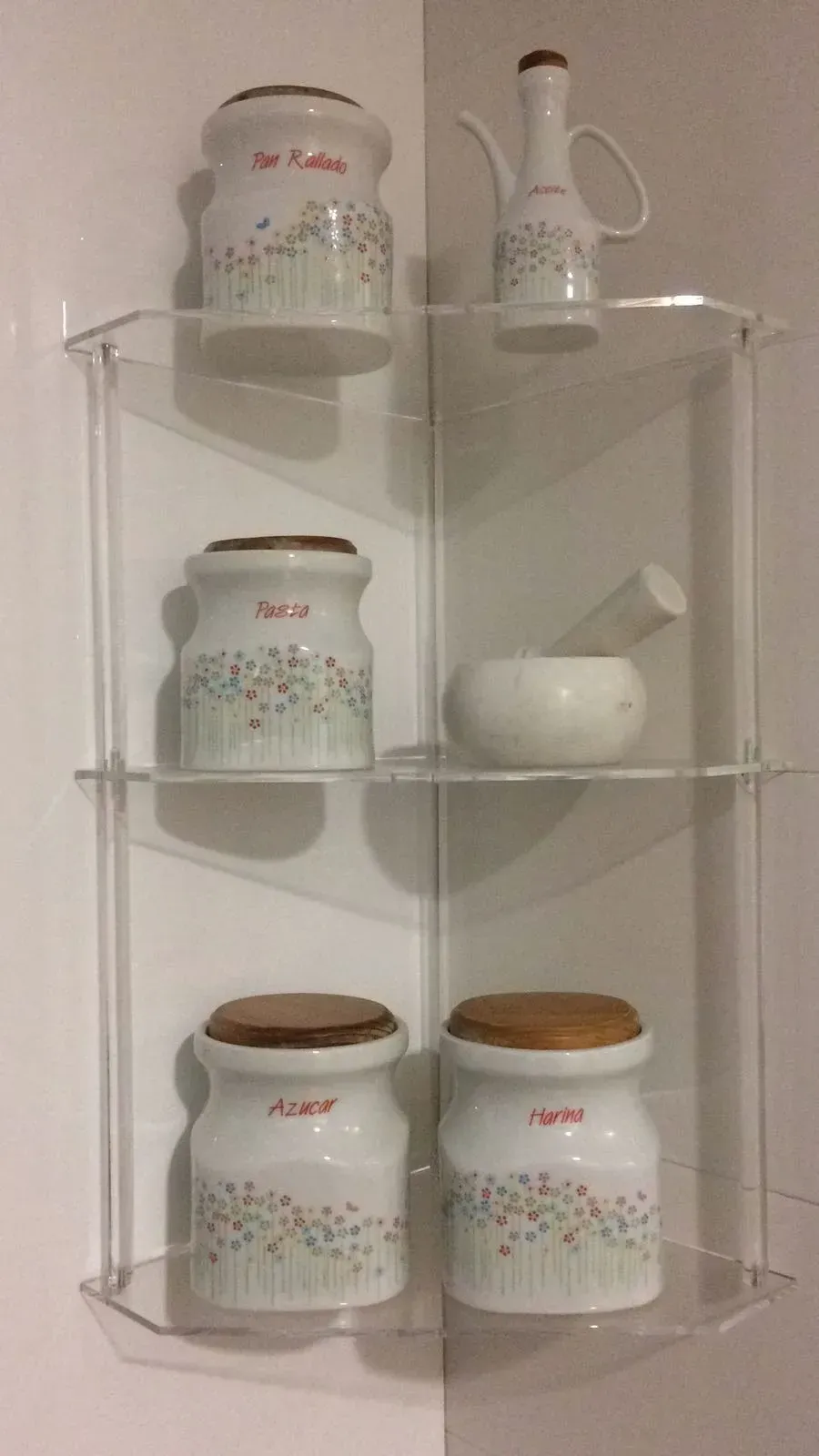 Un estante transparente con frascos y un mortero sobre él.