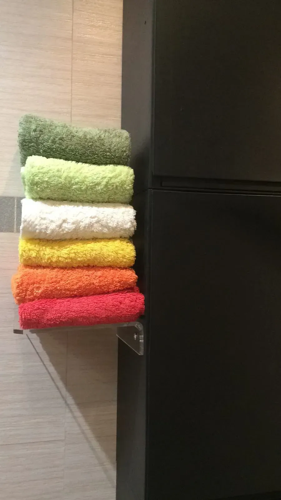Una pila de toallas de colores colgadas en un estante al lado de un refrigerador negro.