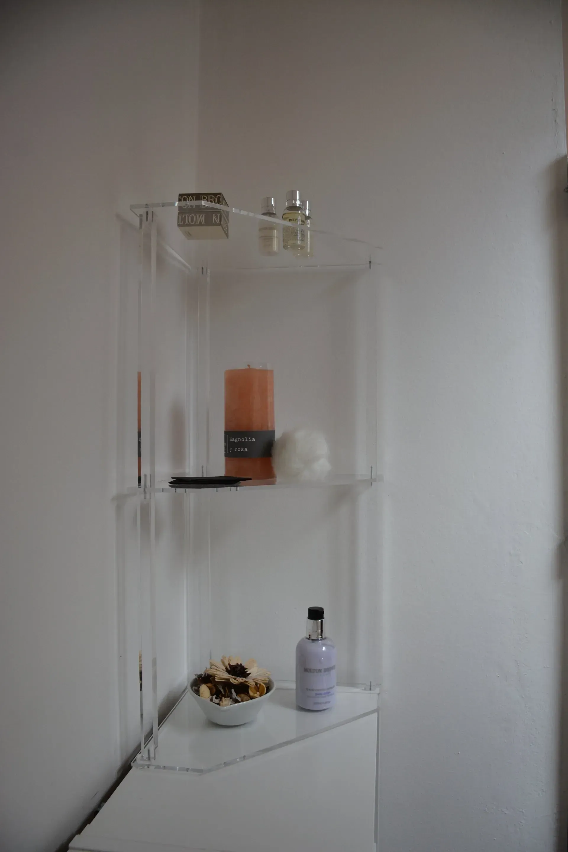 Un estante transparente con velas y botellas encima.