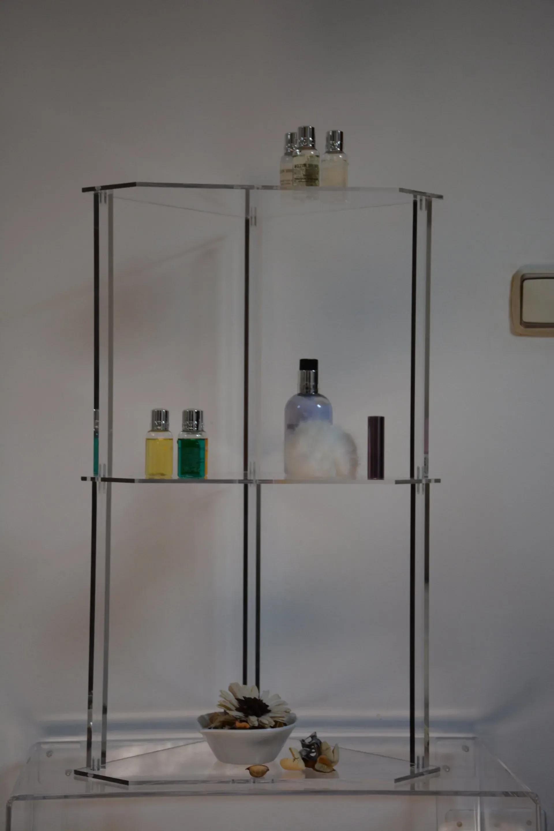 Un estante transparente con botellas de perfume encima.