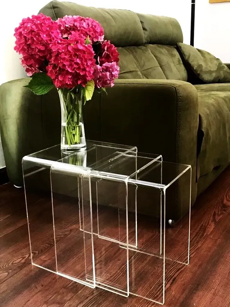 Un jarrón de flores rosas reposa sobre una mesa transparente frente a un sofá verde.