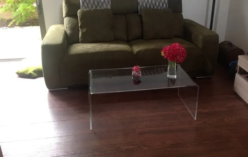 Una sala de estar con un sofá y una mesa de centro transparente.