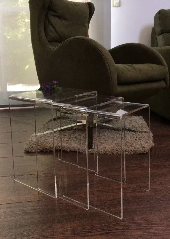 Tres mesas de acrílico transparente están en una sala de estar al lado de una silla.