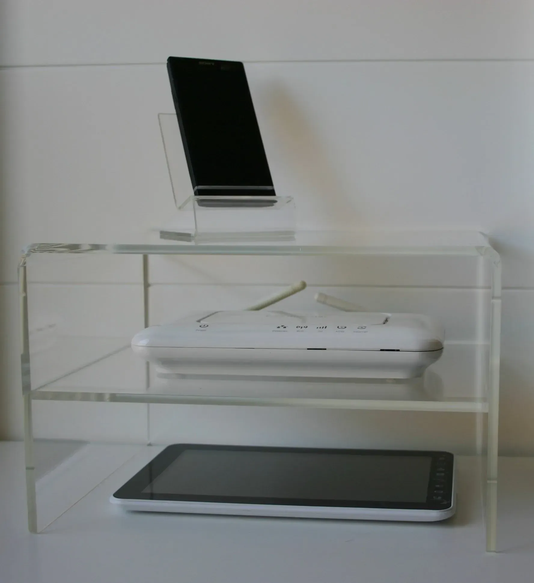 Un estante transparente con un teléfono y una tableta encima.