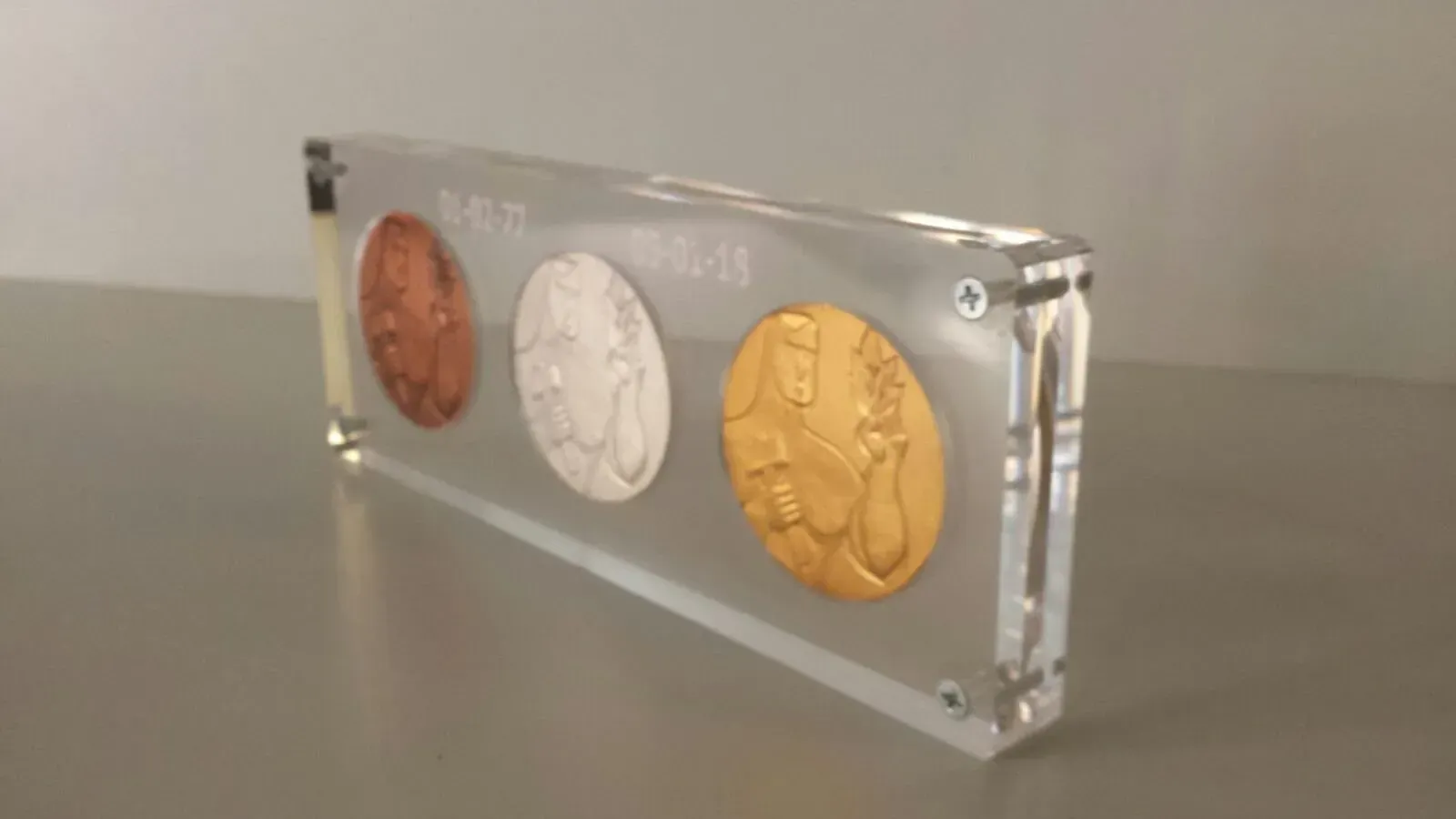 Se muestran tres monedas en un marco de acrílico transparente.