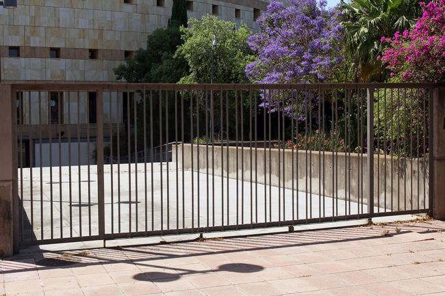 Una puerta corrediza está abierta frente a un edificio con flores violetas al fondo.