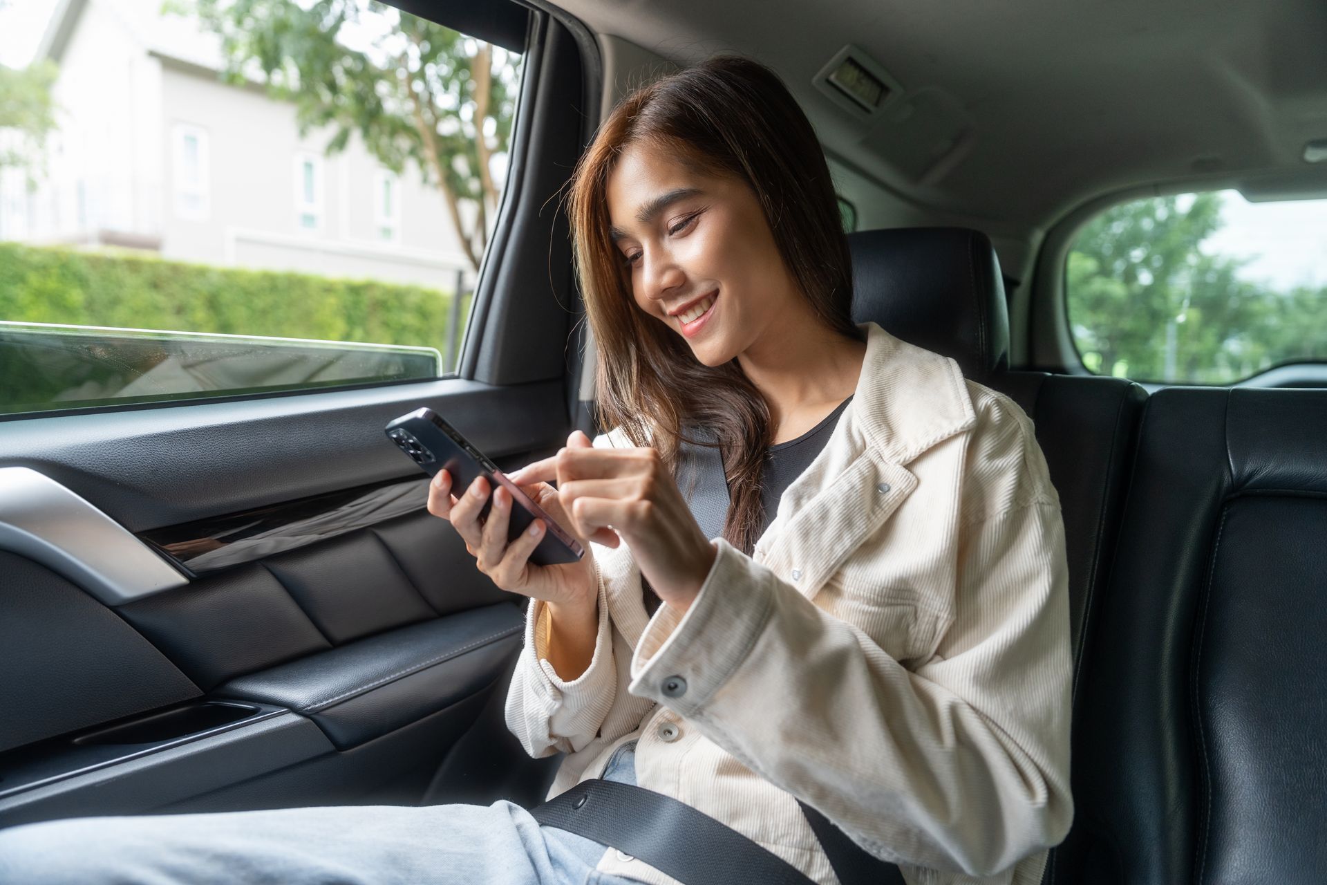 Une femme souriante utilise un téléphone sur le siège arrière d'une voiture.