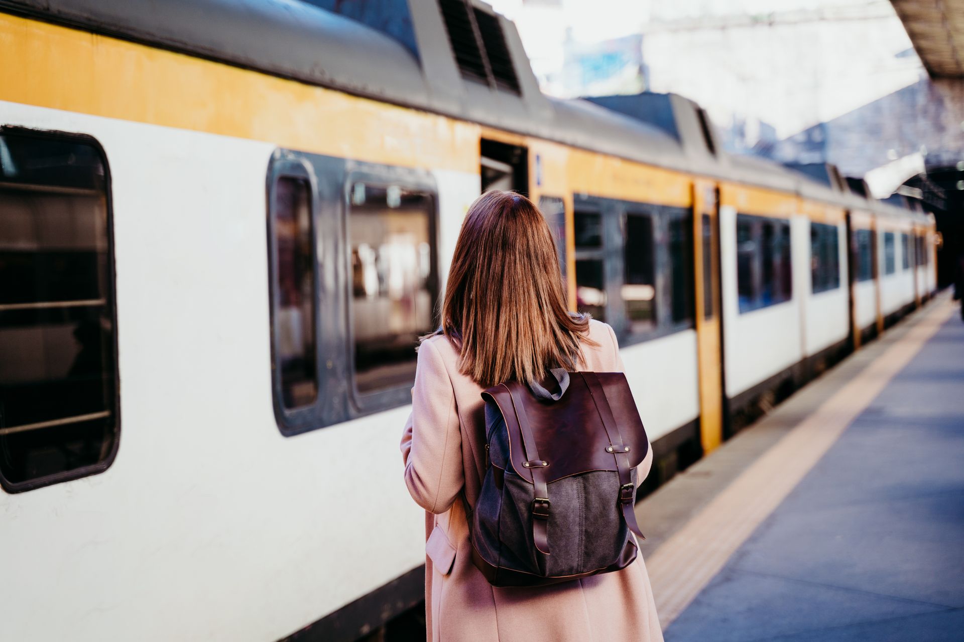 Une femme avec un sac à dos attend près d'un train sur un quai ; wagons blanc et jaune.