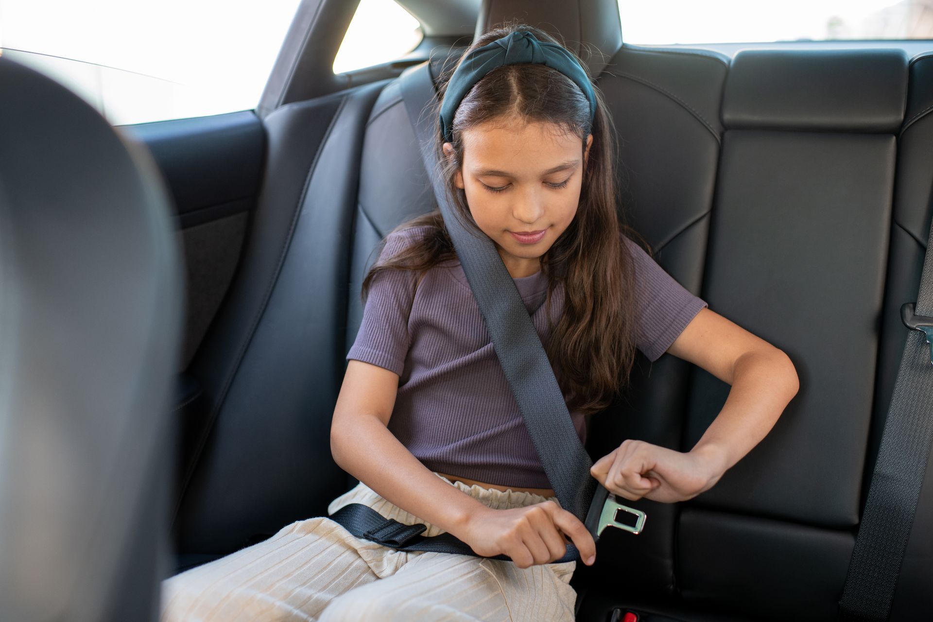 Deux enfants souriants, assis à l'arrière d'une voiture, ceinture de sécurité attachée. L'un d'eux salue, un casque à la main.
