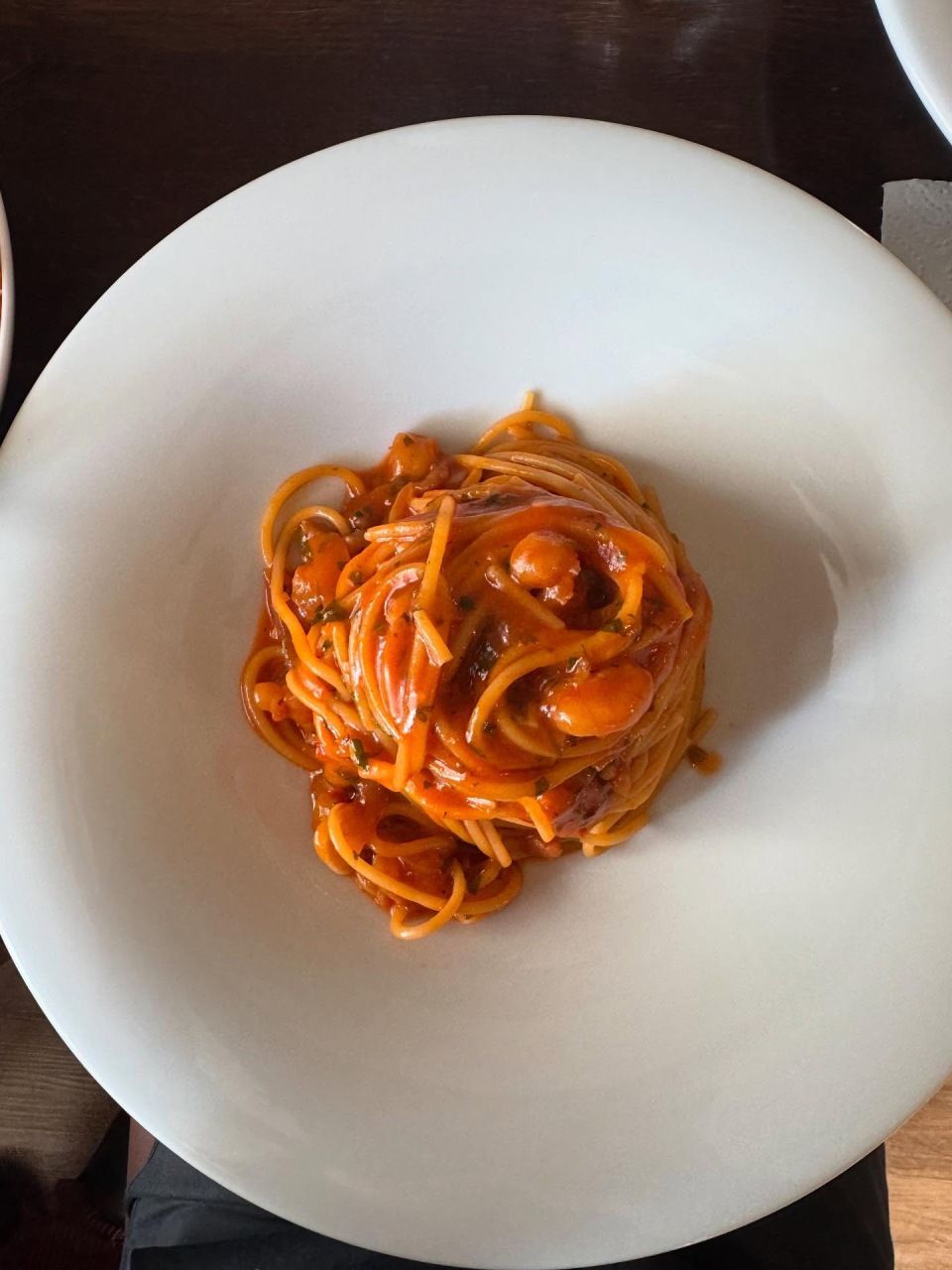 Spaghetti mit roter Sosse und kleinen Fleisch- oder Gemüsestücken in einer weissen Schüssel.