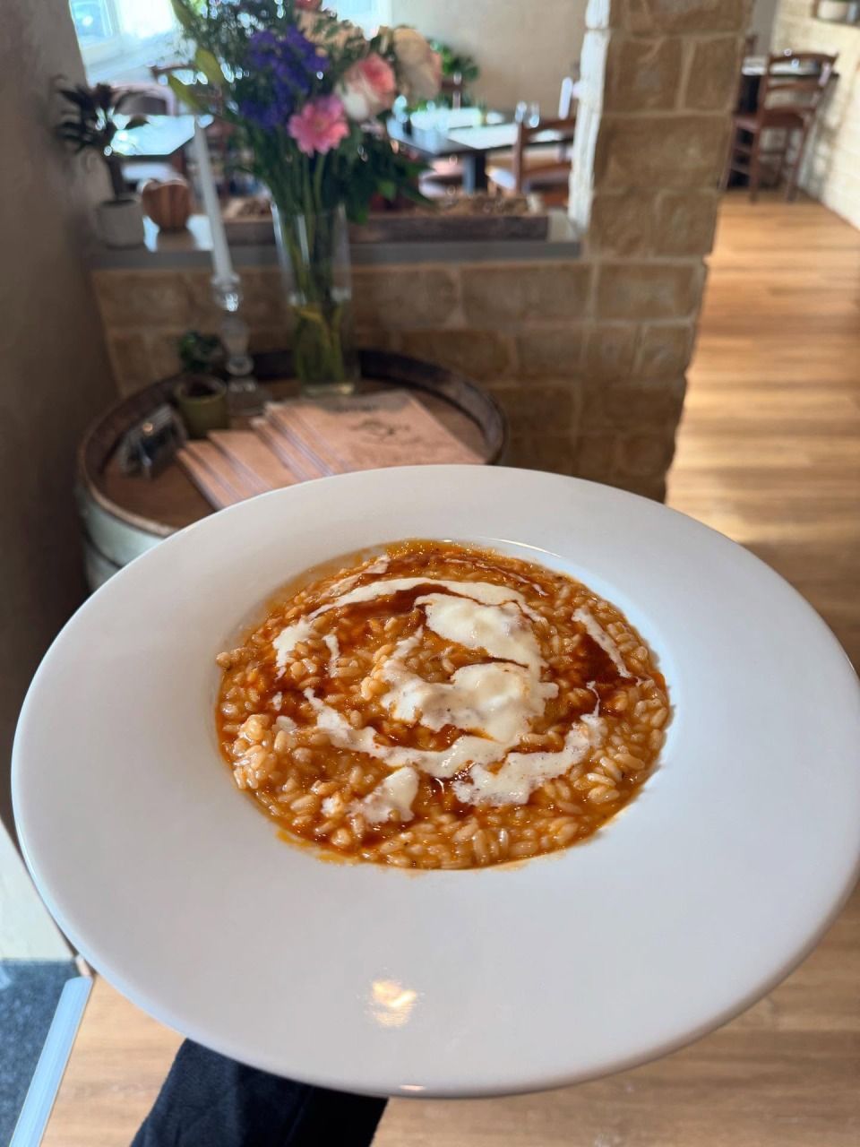 Risotto in einer weissen Schüssel, mit Käse und Sauce überbacken. Drinnen serviert, neben einer Blumenvase.