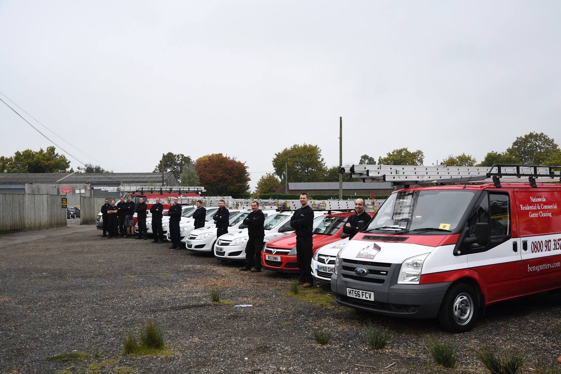 Row of red and white police vans parked in a lot under an overcast sky