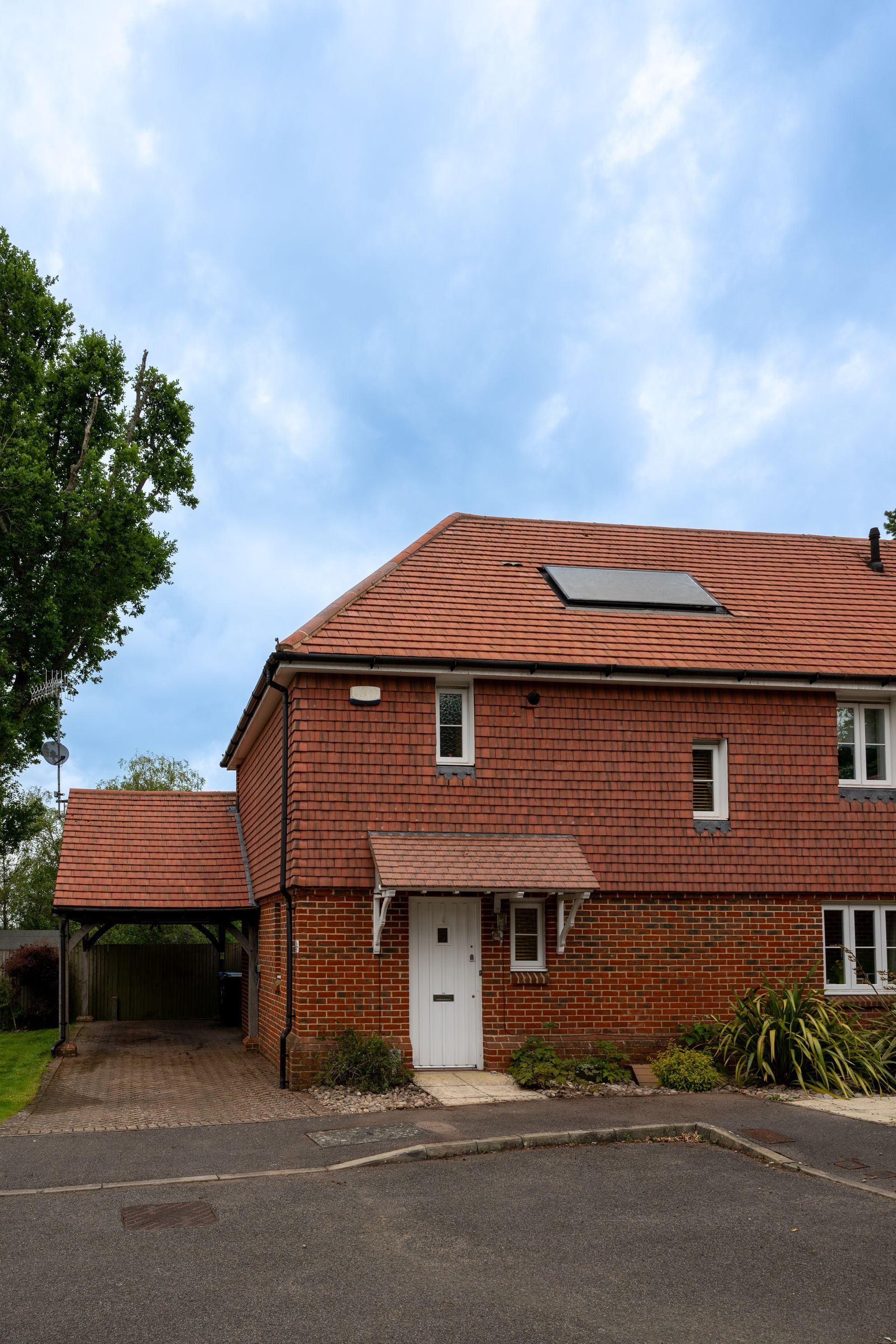 Red brick house with a white door, tiled roof, and skylight under a blue sky