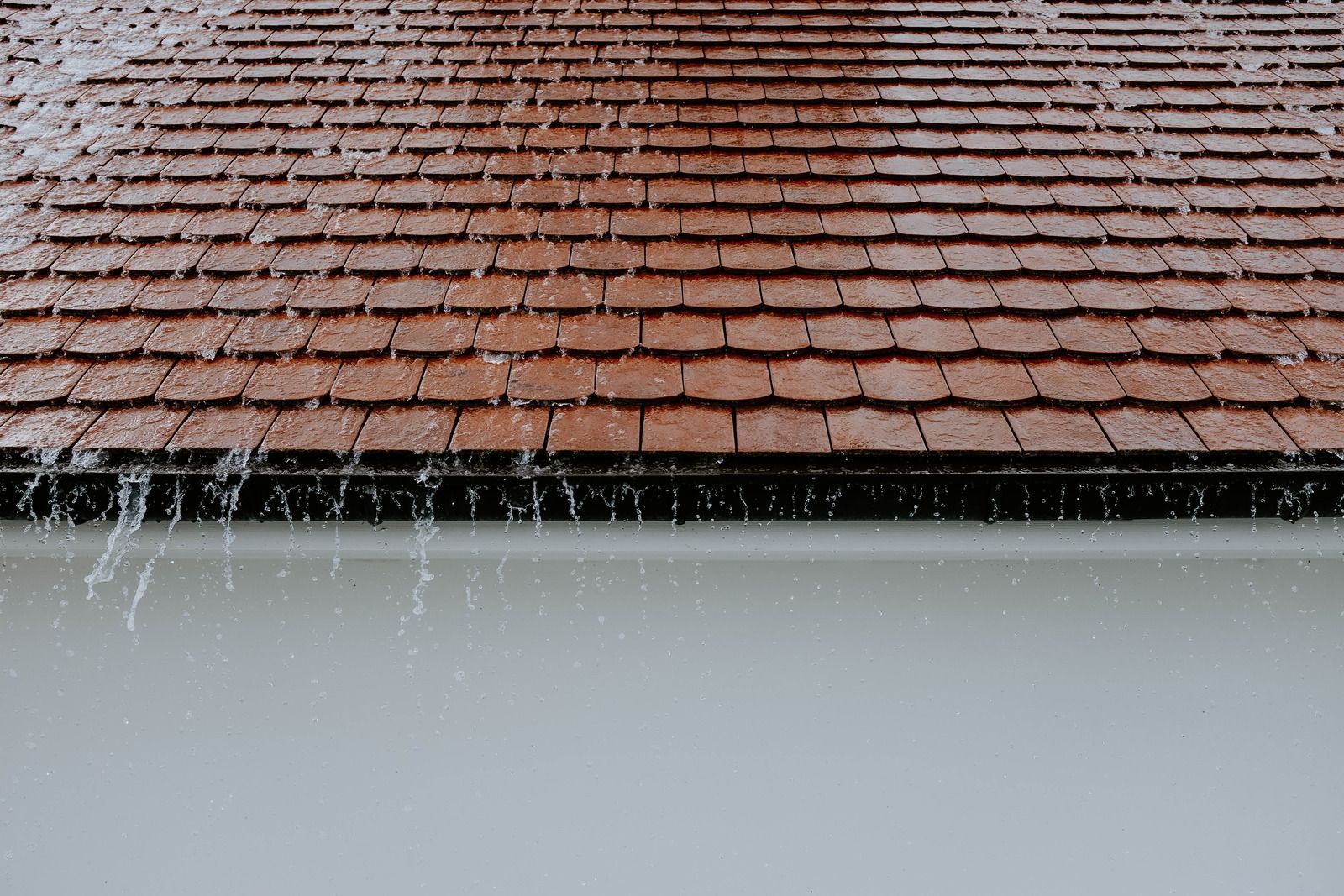 Rainwater streaming off a red tiled roof above a white wall