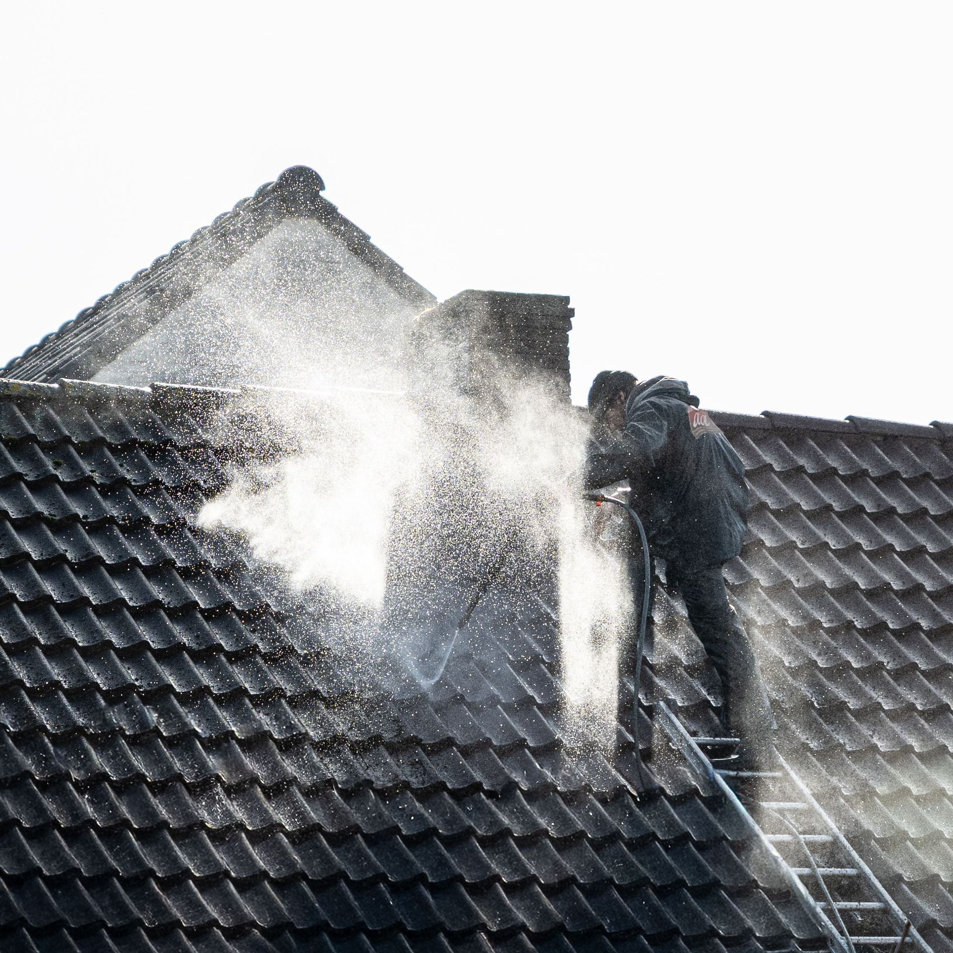 Firefighters spraying water on a house roof as smoke rises from the shingles