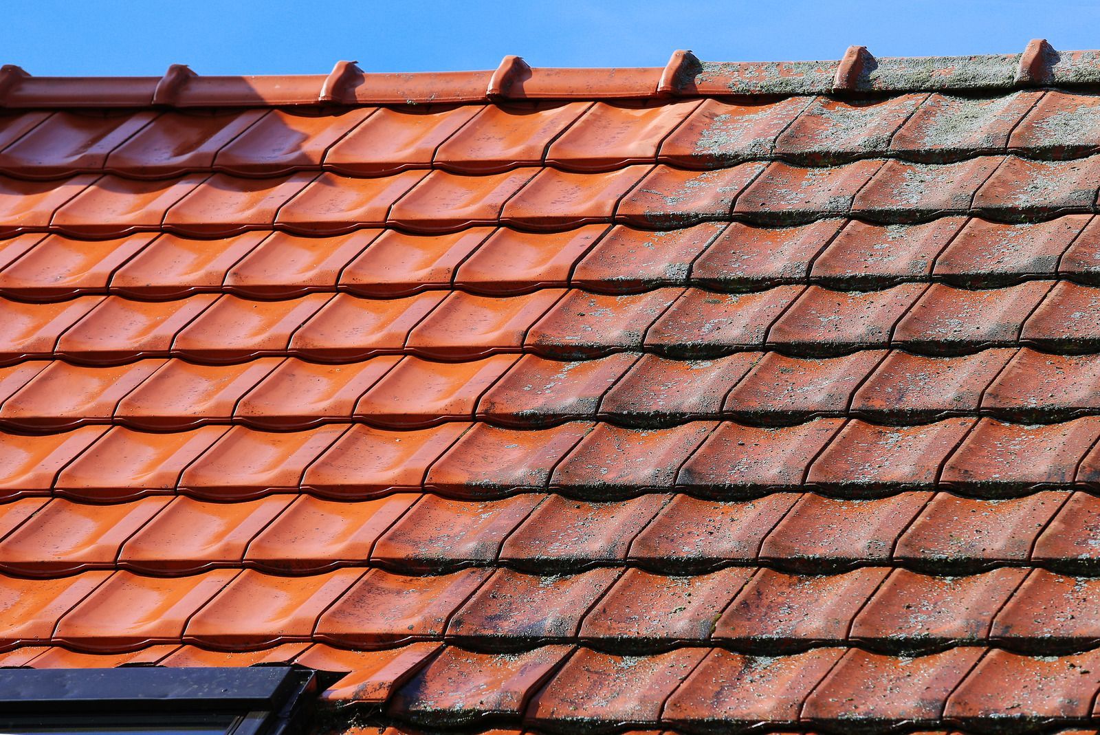 Red clay roof tiles with patches of moss and weathering, seen in close-up.