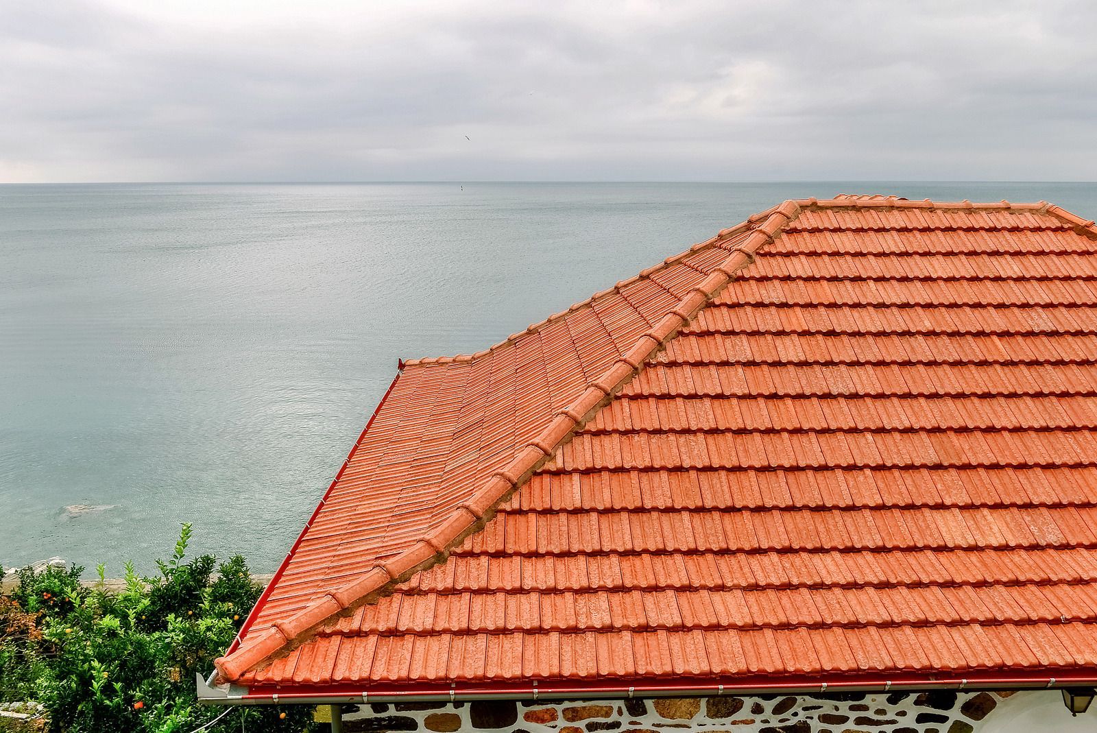 Red-tiled roof beside a calm sea under a cloudy sky