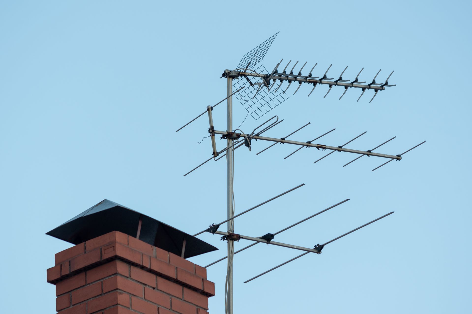 Antennes TV installées sur un toit à côté d'une cheminée en brique rouge