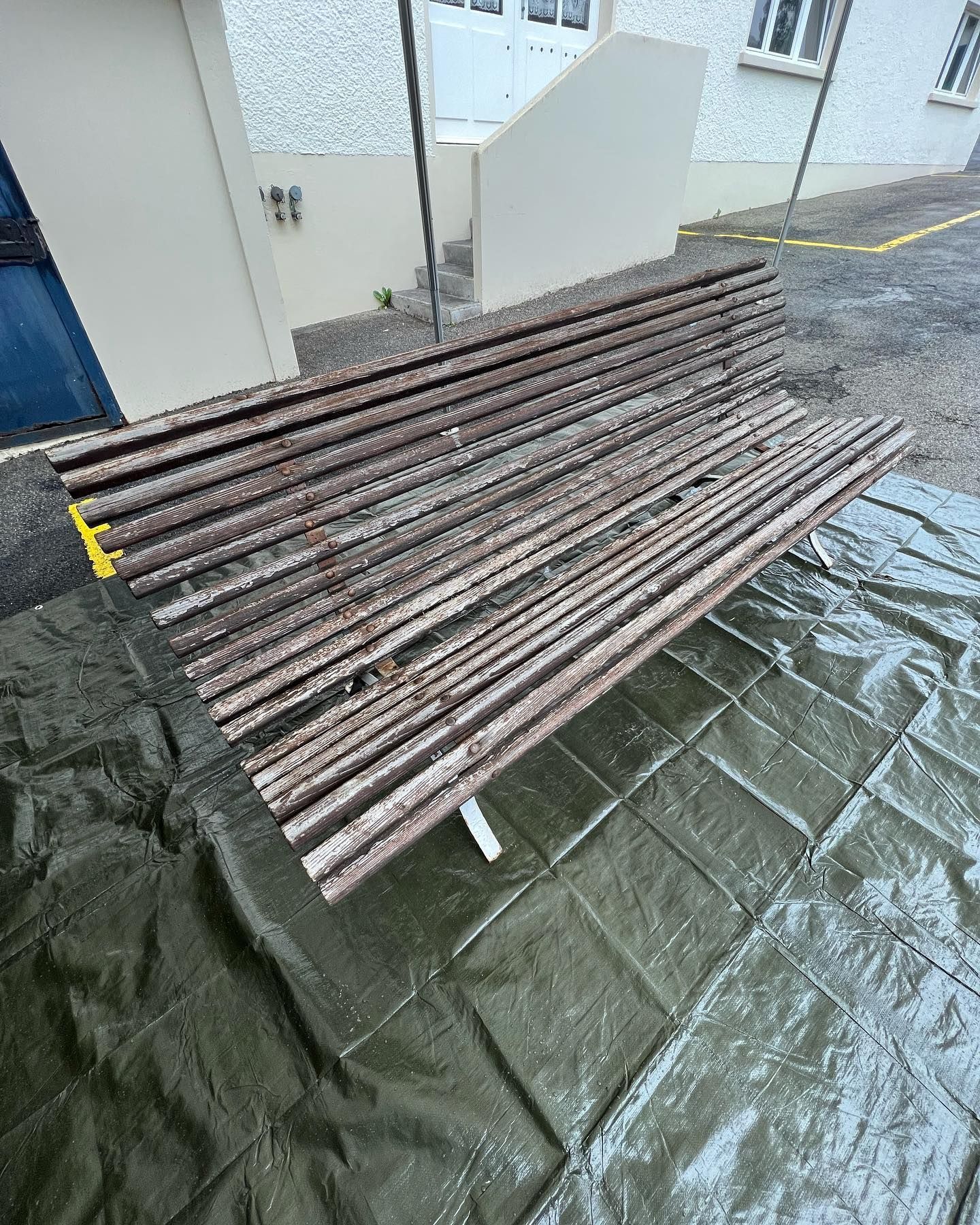 Un banc en bois est posé sur une bâche devant un bâtiment | Giovannini Plâtrerie-Peinture Sàrl