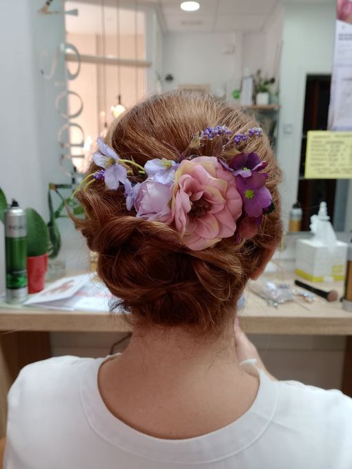 Vista trasera de un peinado recogido adornado con flores rosas y moradas en el espejo de un salón de belleza.