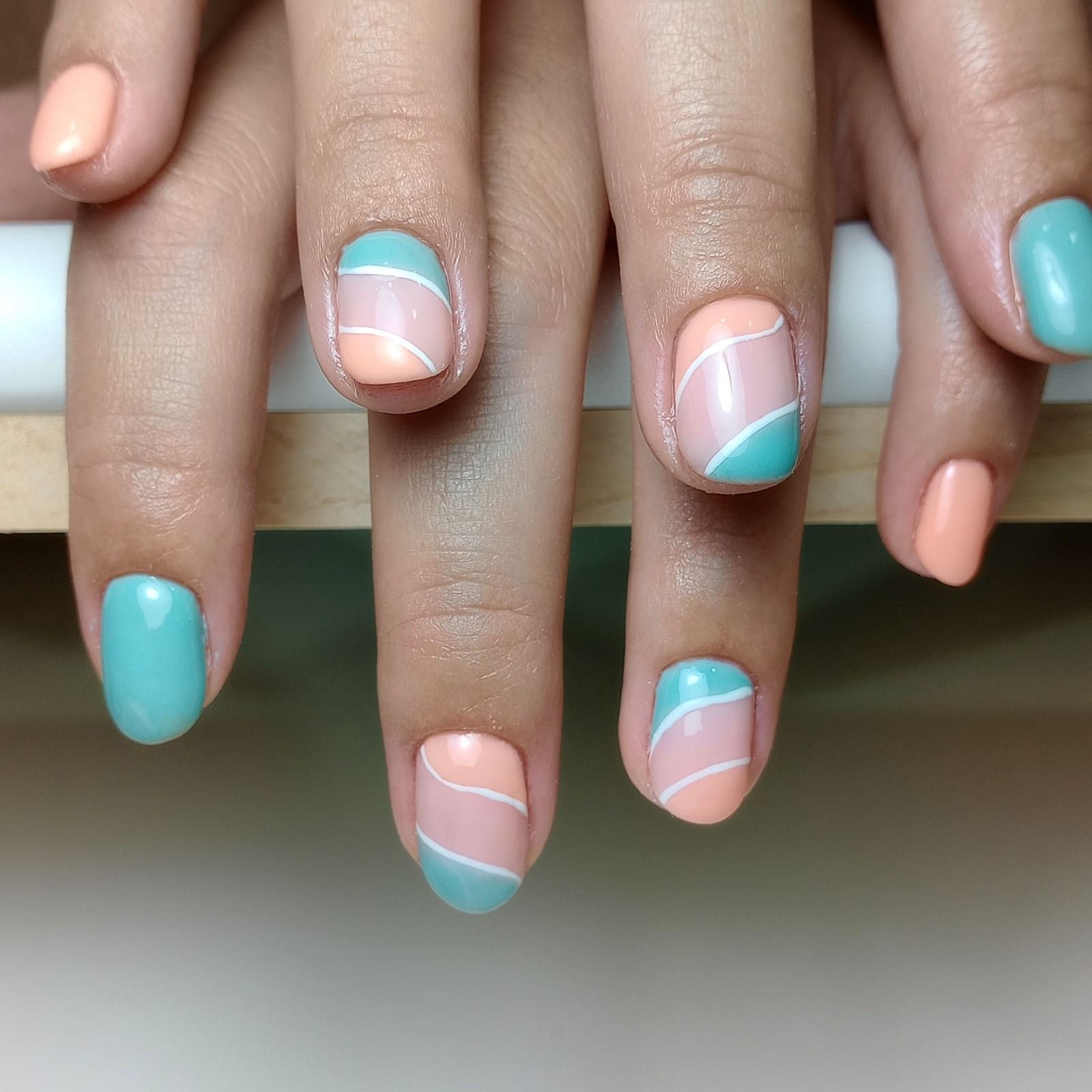 Manicura en tonos turquesa pastel y melocotón, con detalles de espirales blancas sobre uñas naturales