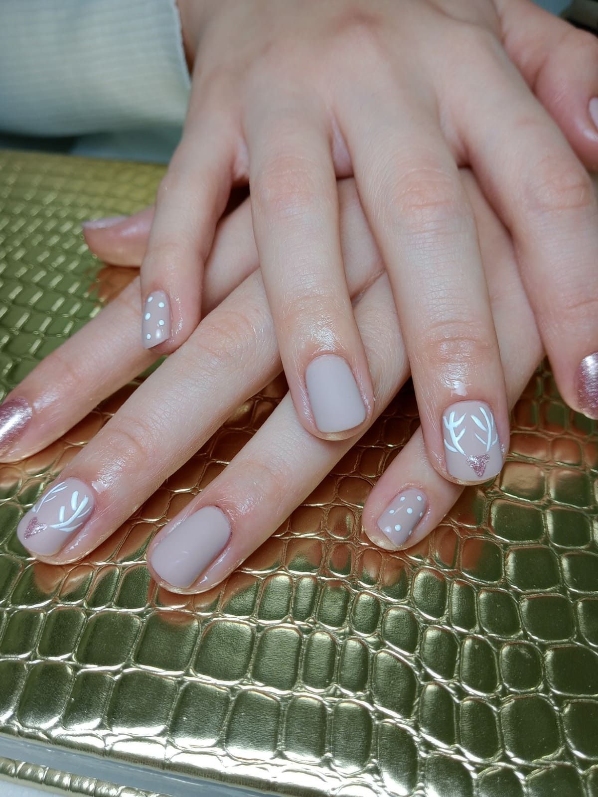 Manos con uñas arregladas de color rosa pálido apoyadas sobre una superficie metálica verde con textura.