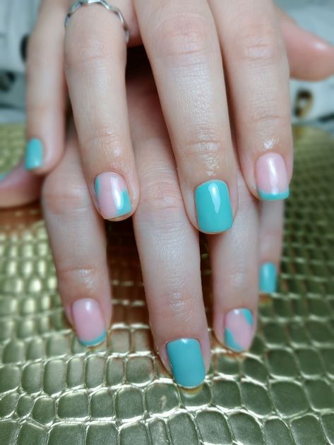 Mano con las uñas pintadas de turquesa y tonos pastel iridiscentes, apoyada sobre una superficie dorada texturizada